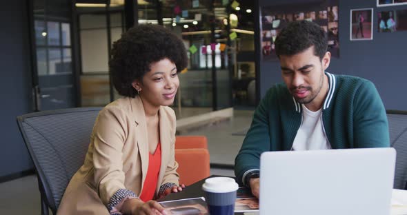 Diverse business people sitting using a laptop high fiving in a modern office