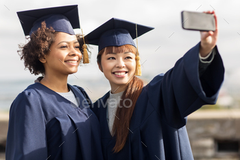 pt – group of happy international students in mortar boards and bachelor gowns taking selfie by smartphone outdoors