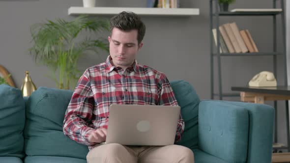 Man with Laptop Showing Thumbs Down on Sofa