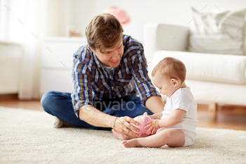 t – happy smiling young father and little baby playing with piggy bank at home