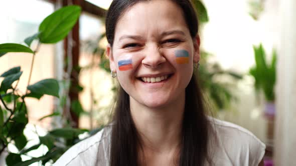 A Young RussianUkrainian Girl with the Flag of Ukraine and Russia on Her Face is Smiling