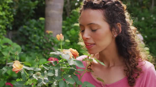 Portrait of happy biracial woman smelling roses in garden