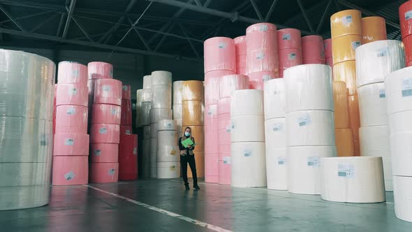 Female Worker Taking Notes in a Warehouse Full of Large Rolls of Paper