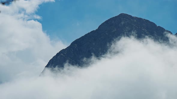 Huge High Rocky Peak on Blue Sky Background Surrounded By Clouds