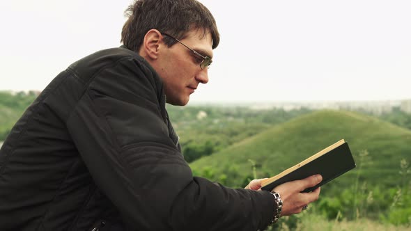 Man Reading Book in Green Hilly Field