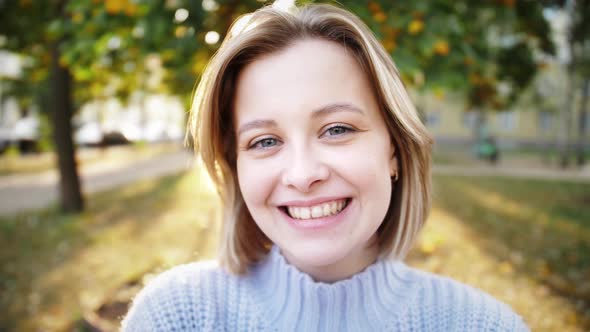 Smiling young model looking at camera, happy beautiful lady posing outdoor autumn in the park.