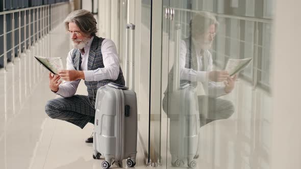 Senior Man Planning Vacation with a Map Sitting at the Airport