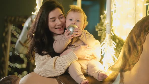 Mom and Baby Play on Carousel with Horses