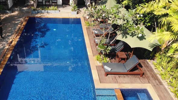 Drone Tilt Shot From Tropical Hotel Swimming Pool to Reveal the Hotel Rooms with Balconies