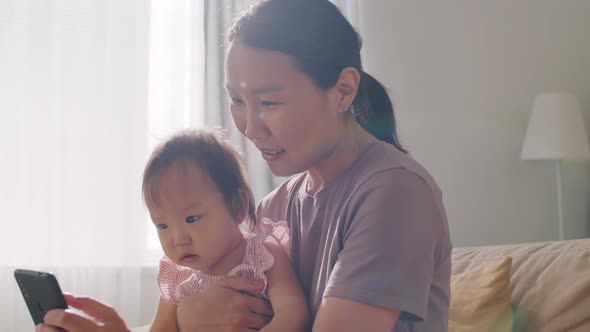 Asian Mom Showing Video on Smartphone to Baby Daughter