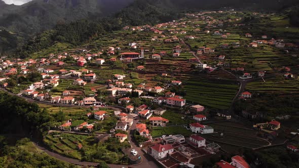 Aerial view of a small village on top of a green hill with terraced houses in a mountain landscape,