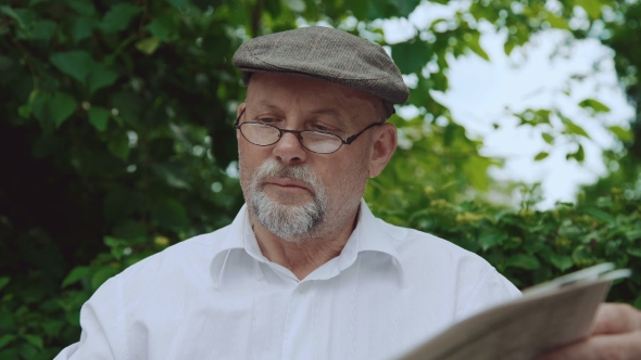 Handsome Senior Man Reading the Newspaper on the Bench in Park