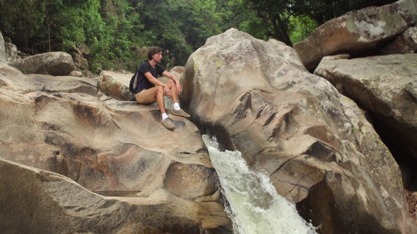 Tourist Sits By a Small Waterfall in Jungles of South-eastern Asia.