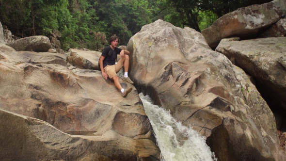 Tourist Sits By a Small Waterfall in Jungles of South-eastern Asia