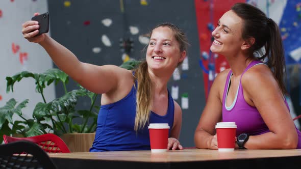 Two happy caucasian women taking selfie with smartphone in cafe at indoor climbing wall