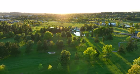 High rotating aerial shot of golf course. Country club green during spring sunset in America.