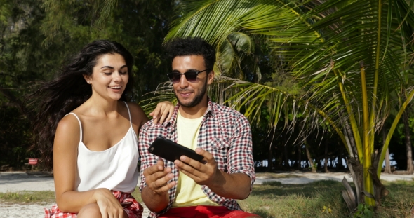 Couple Using Cell Smart Phone Take Selfie Photo Outdoors Under Palm Trees On Beach, Happy Smiling