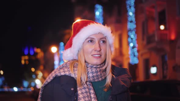 a woman chatting on her smartphone wearing a Santa hat is a night city.