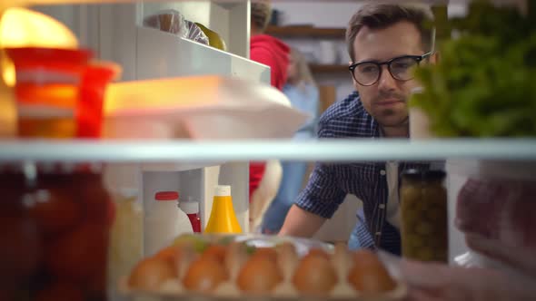 Young Handsome Man Opening Fridge and Taking Container with Food