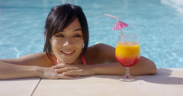 Happy Young Woman Eyeing a Large Tropical Cocktail