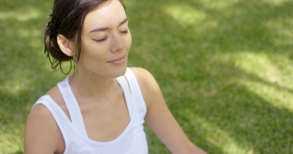 Serene Young Woman Meditating on a Green Lawn