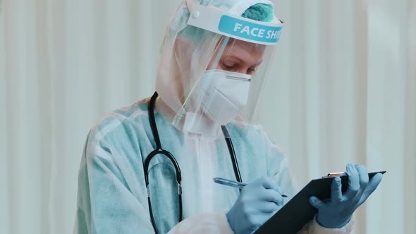 Woman Doctor with Hazmat, Protective Mask and Face Shield Writing Patient Notes