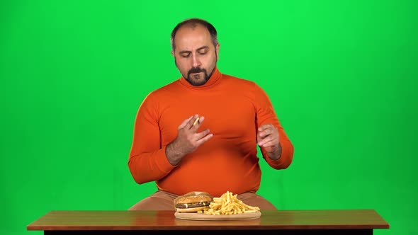 Man with Overweight Looks at Delicious Junk Foods on the Table Then Playing with French Fries, Green