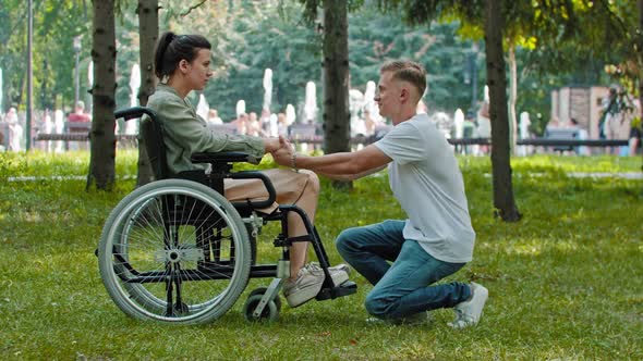 Alone Woman Sitting in a Wheelchair in the Park and Her Boyfriend Comes Up to Her and Holds Her