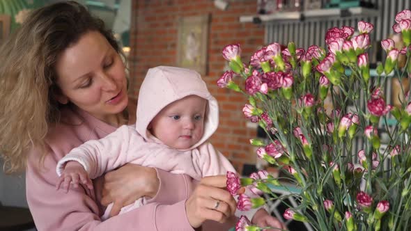 Beautiful Young Mother Showing Pink Flowers To Her Baby Daughter Indoors.