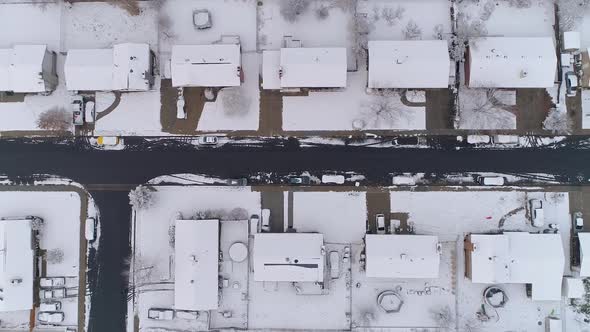Slowly flying over snow covered houses looking down at street