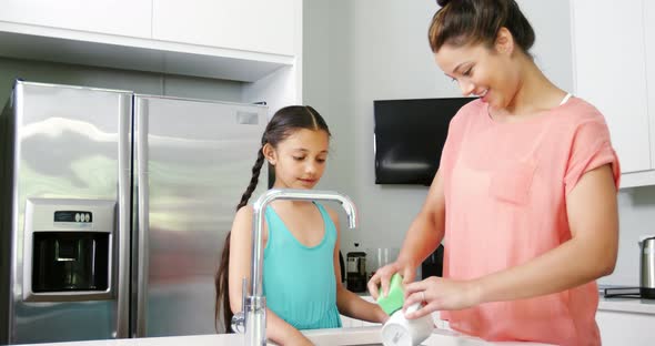 Mother teaching daughter to washing crockery in kitchen