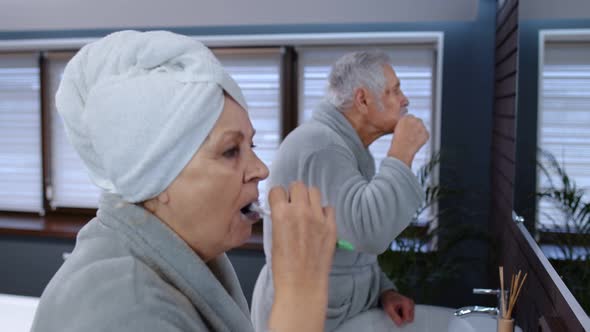 Senior Couple Grandmother and Grandfather Brushing Teeth and Looking Into a Mirror at Bathroom