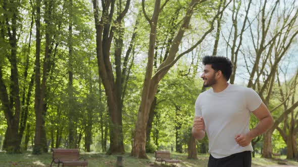 Happy Muscular Man Dressed in Sport Clothes Jogging During Morning Time at Green