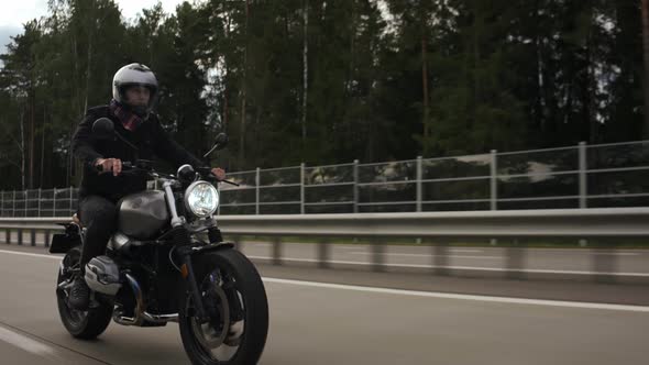 Man Riding Scrambler Motorbike on the Highway Through the Forest Side View