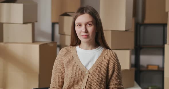 Beginner Entrepreneur Woman Is Standing in Her Warehouse with Handmade Goods Against Cardboard Boxes