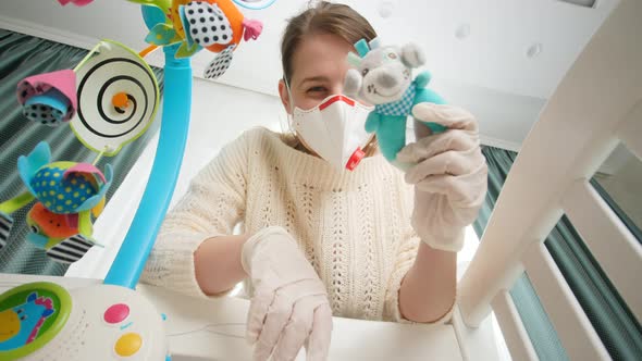 Mother in Medical Respirator Mask Playing Toys with Her Baby Lying in Bed