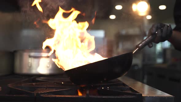 Chef tosses vegetables in pan producing flames over oven.