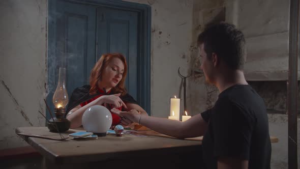 Soothsayer Palm Reading To Man in Rustic House