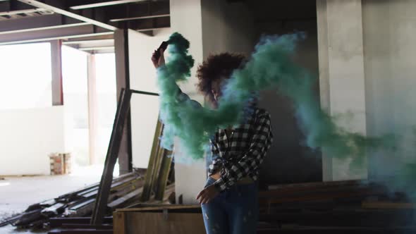 Mixed race woman holding green flare dancing in an empty building