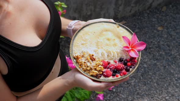 Hands Holding Banana Fruit Smoothie Bowl Served with Berries and Granola