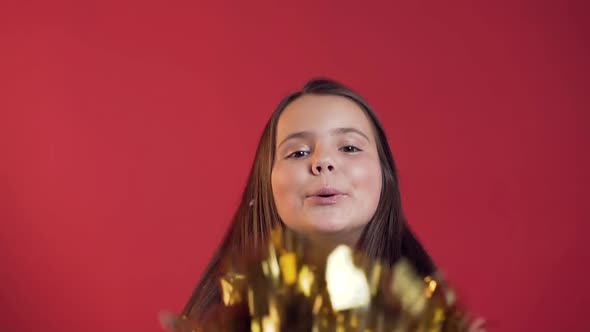 Adorable Cheerful Little Girl with Braces Blowing Golden Confetti to the Camera