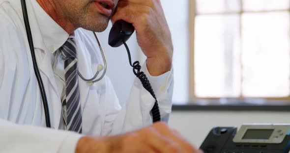 Physician using laptop while talking on landline at desk in clinic