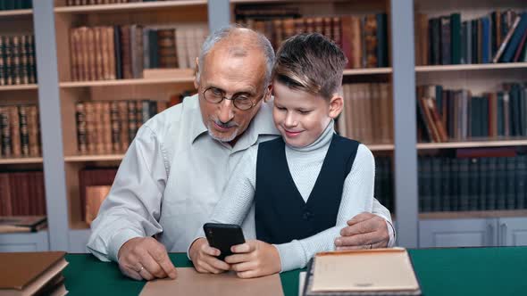 Happy Grandfather and Grandson Chatting Use Smartphone Together Surfing Internet Studying at Library