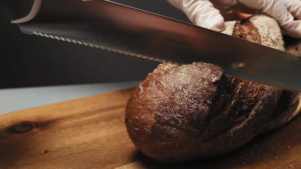 Woman Cuts Loaf of Fresh Rye Bread on Wooden Board Macro