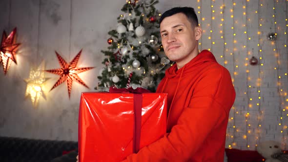 Young Handsome Man with Big Wrapped Gift on Background of Christmas Tree