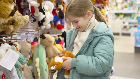 a Happy Little Girl Chooses a Plush Toy in a Children's Store