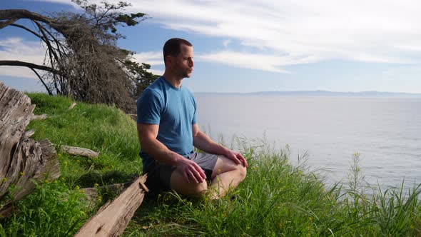 A man sitting in a meditation pose practicing deep breathing exercises and mindfulness on a beach cl