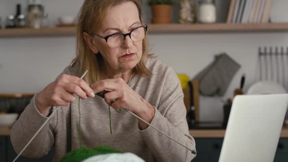 Senior caucasian woman at home learning how to knit from video tutorial.