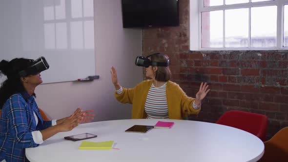 Happy diverse female business colleagues sitting at table using vr headsets in meeting room