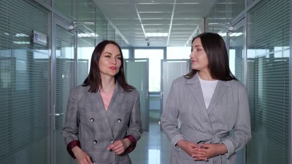 Stylish Businesswomen in Grey Jackets Walk Along Hallway